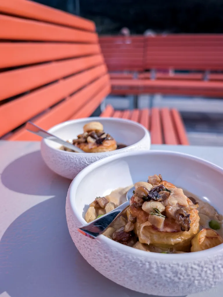 Two white bowls with mushroom-shaped pastries and spoons on a table; in the background, orange benches on a ship