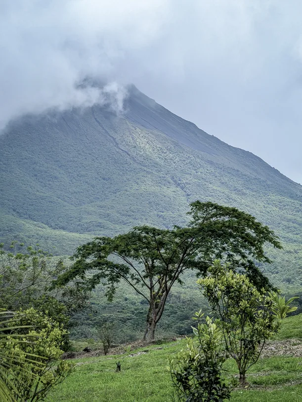 The Arenal volcanic cone rises out of lush green tropical vegetation while clouds drift around its summit