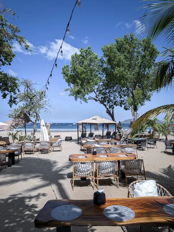Elegant beach restaurant with wooden tables and rattan chairs under palm trees directly on the Pacific beach of Tamarindo