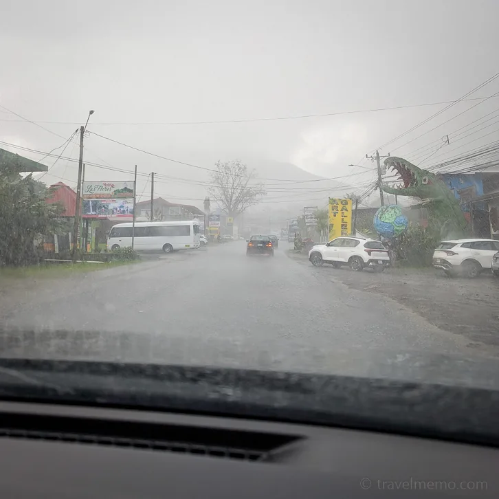 blick durch eine regennasse windschutzscheibe auf eine dorfstrasse in costa rica mit parkierten fahrzeugen und geschäften bei starkem regen