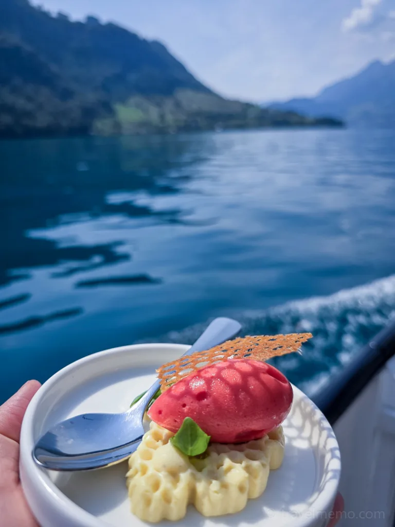 A small dessert creation featuring berry sorbet and a waffle on a plate, with a lake and mountains in the background