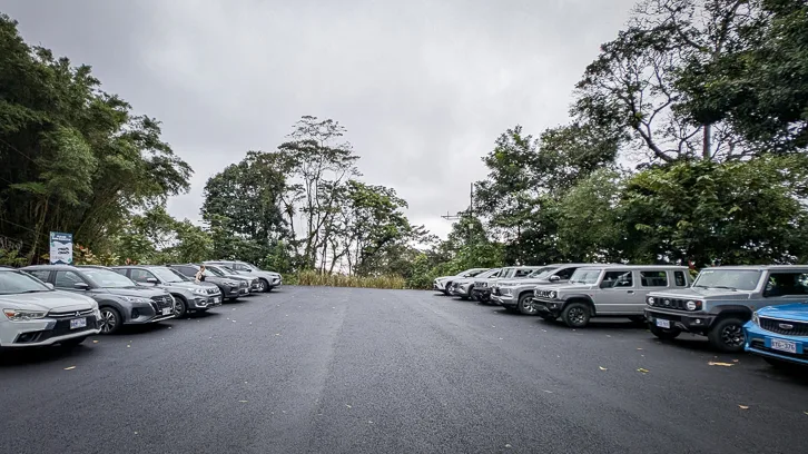 Asphalted parking lot with many parked cars surrounded by dense tropical rainforest under a cloudy sky