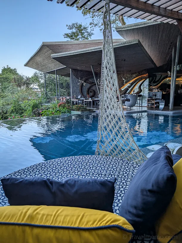 Macanda by the Sea Infinity pool with hammock in the foreground, behind it modern hotel architecture with open areas and tropical vegetation.