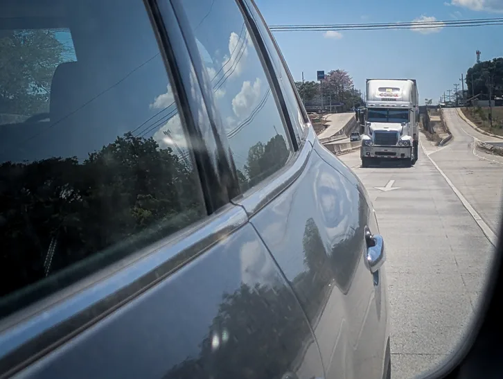 View out of the car window onto a highway with a truck and hilly landscape in the background