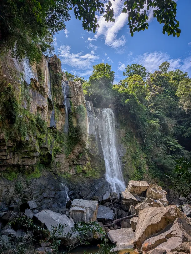 The Upper Nauyaca Waterfall plunges down a rock face covered in vegetation, surrounded by tropical flora, onto large boulders.