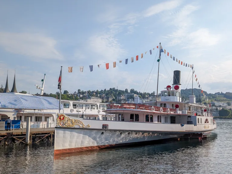 The historic steamship Gallia, adorned with colorful signal flags, is docked at the pier in Lucerne on Lake Lucerne