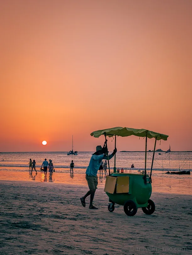 Beach vendor with colorful ice cream cart at sunset on Tamarindo beach, people in the background by the water