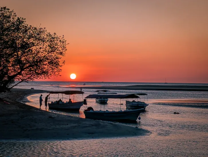 Fishing boats on Tamarindo beach at sunset with orange-red sky and silhouettes of people
