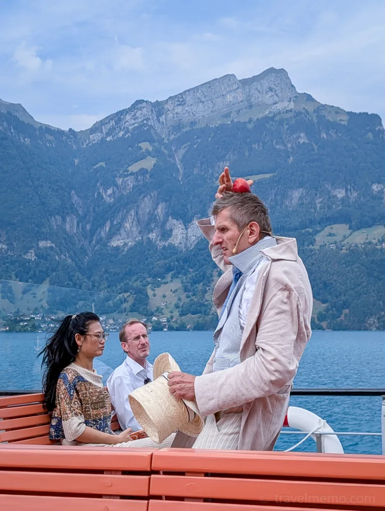 A person in an unusual costume stands on a boat overlooking Lake Lucerne and the surrounding mountains