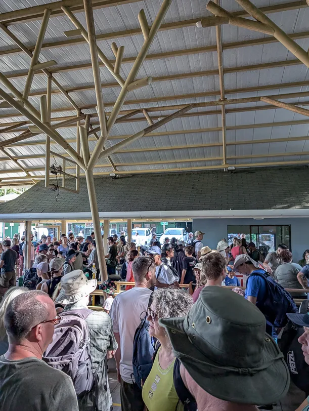 Large crowds of tourists under a covered wooden structure in front of the Manuel Antonio National Park visitor center